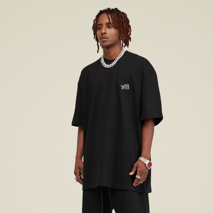 A person in front wearing the Blackness Emancipate T-shirt with WB logo on front. - WEAREBLACKNESS.COM