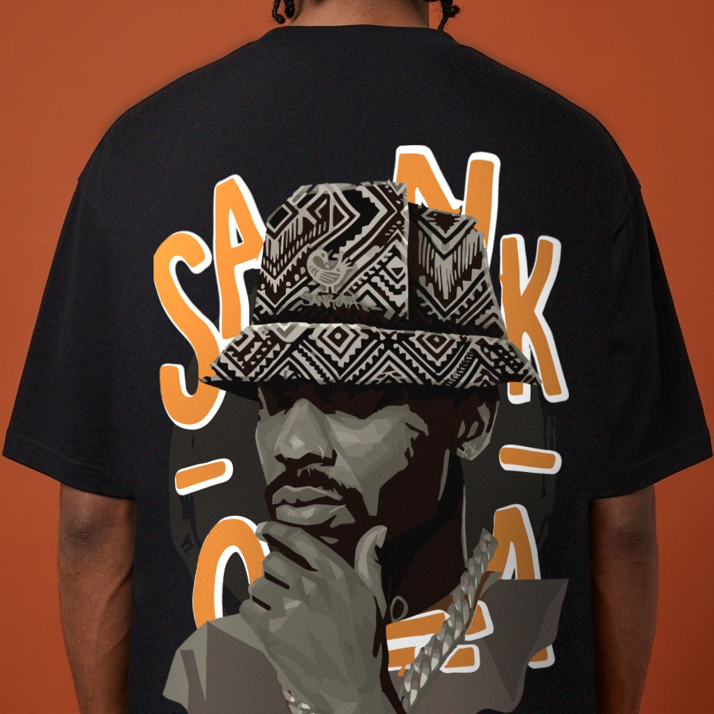 Blackness Sankofa King Tee, black — close-up of the Sankofa back print worn, terracotta backdrop