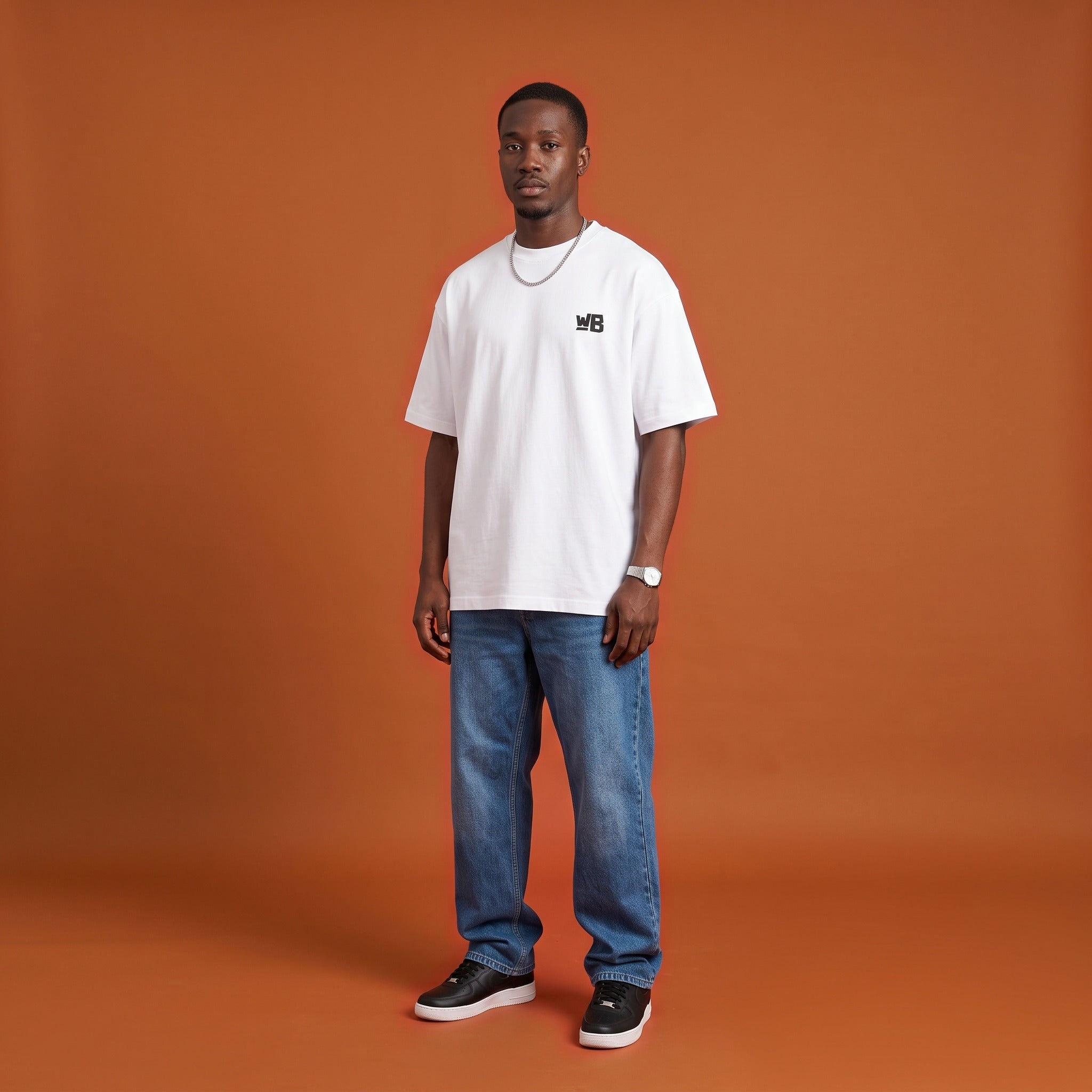 Blackness Sankofa King Tee, white, worn by a model — front view with WB chest logo, burnt-orange terracotta studio backdrop
