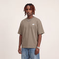 Base Blackness Tee Brown worn by model, front view with WB chest logo on warm ivory studio backdrop