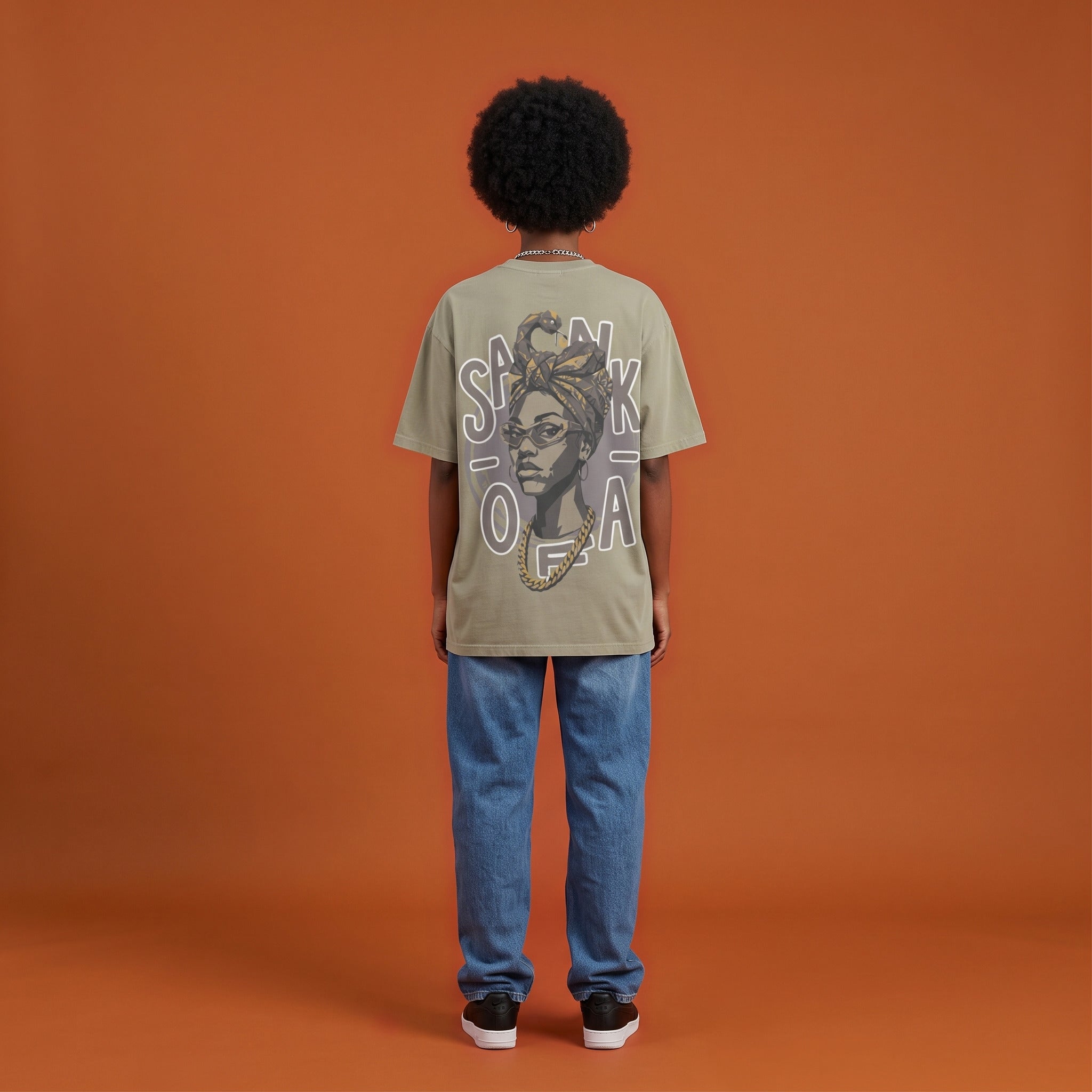 Blackness Sankofa Queen Tee, brown khaki, worn by a model — back view, Sankofa headwrap portrait print, terracotta backdrop