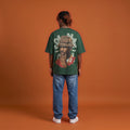 Blackness Sankofa King Tee, deep forest green, worn by a model — back view, Sankofa woven hat portrait print, terracotta backdrop