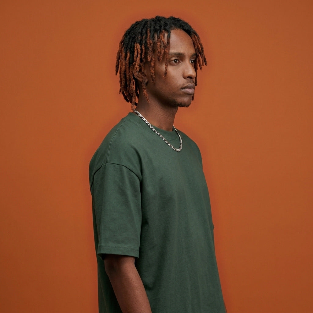 Blackness Sankofa King Tee, deep forest green — shoulder and collar detail, side view, terracotta backdrop