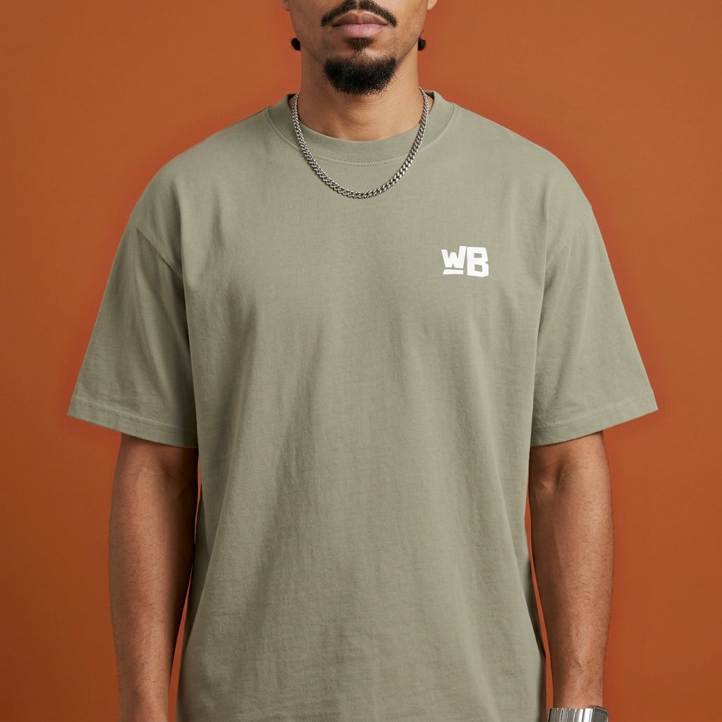 Blackness Sankofa King Tee, brown khaki — chest detail close-up with WB monogram and ribbed collar, terracotta backdrop
