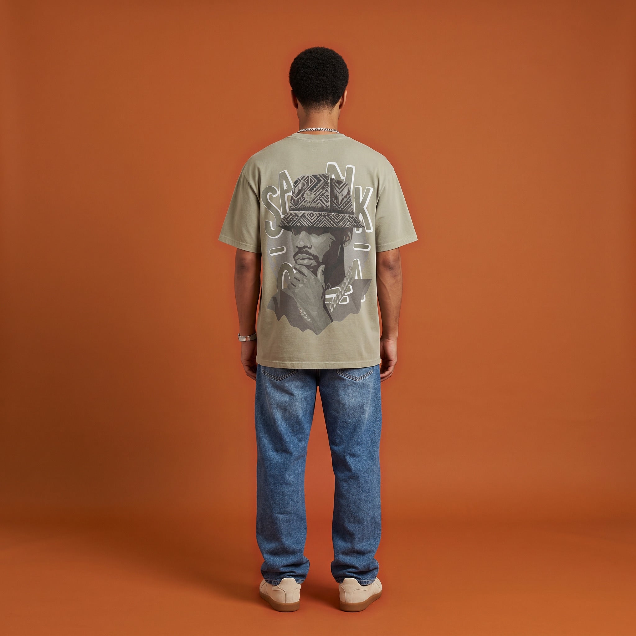 Blackness Sankofa King Tee, brown khaki, worn by a model — back view, Sankofa woven hat portrait print, terracotta backdrop