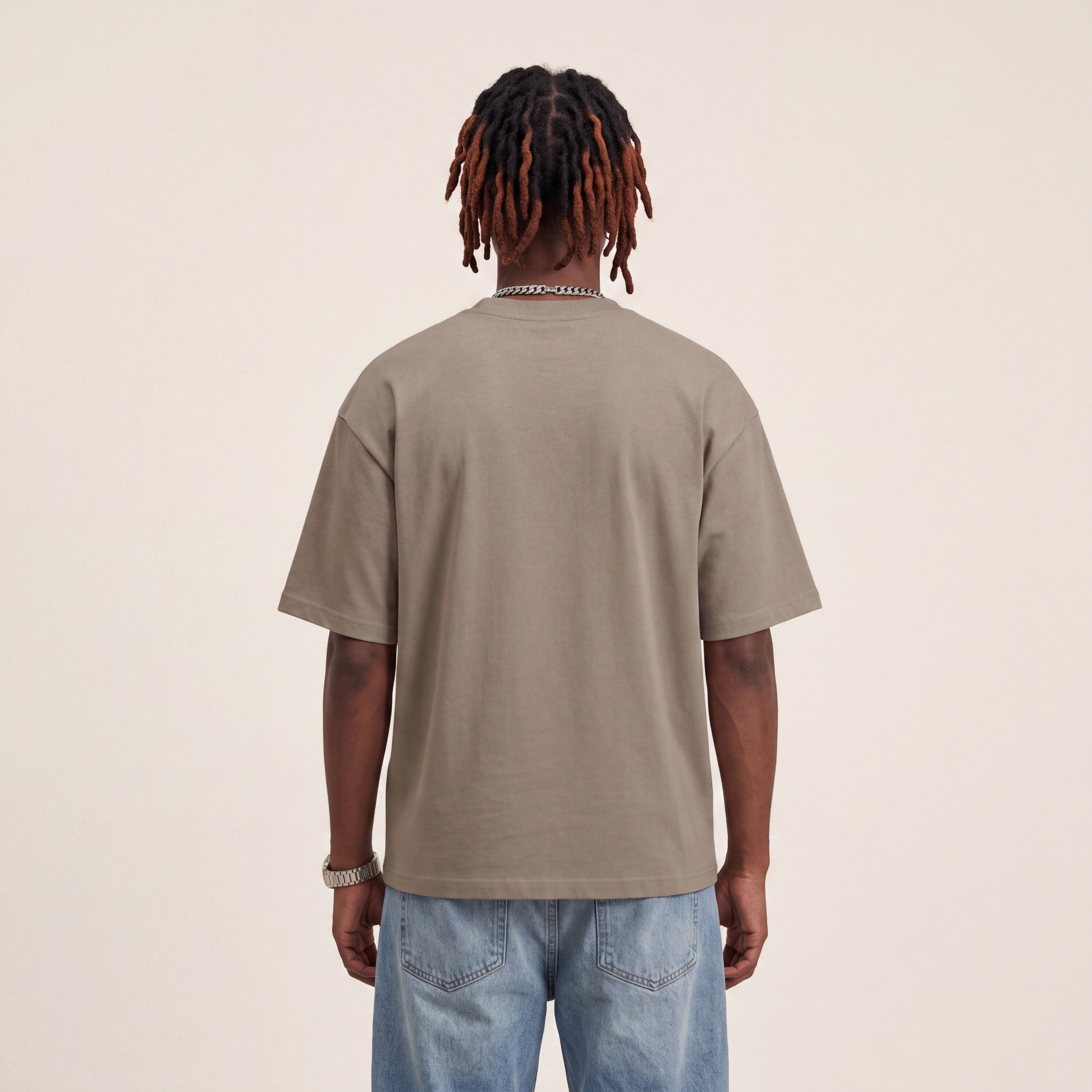 Base Blackness Tee Brown worn by model, back view showing the clean plain back on warm ivory studio backdrop