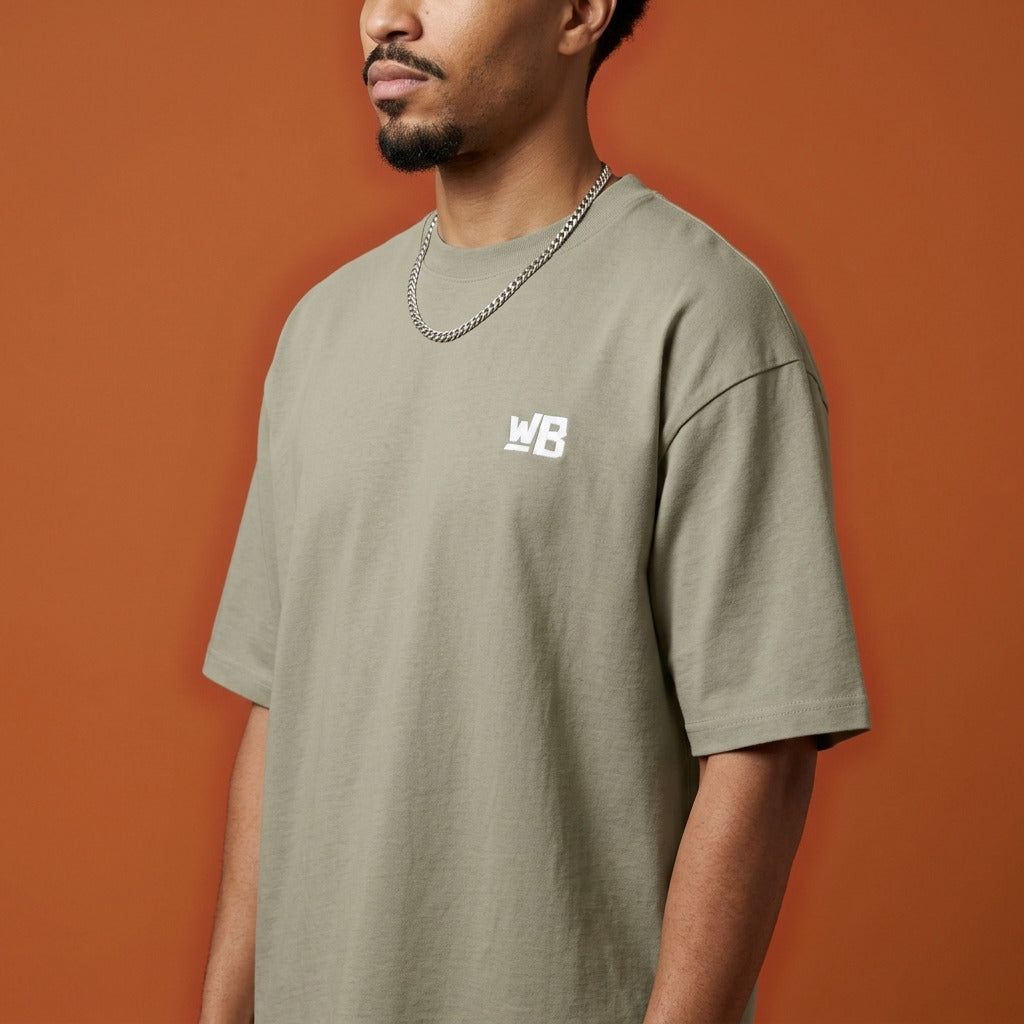 Blackness Sankofa King Tee, brown khaki — shoulder and collar detail, side view, terracotta backdrop