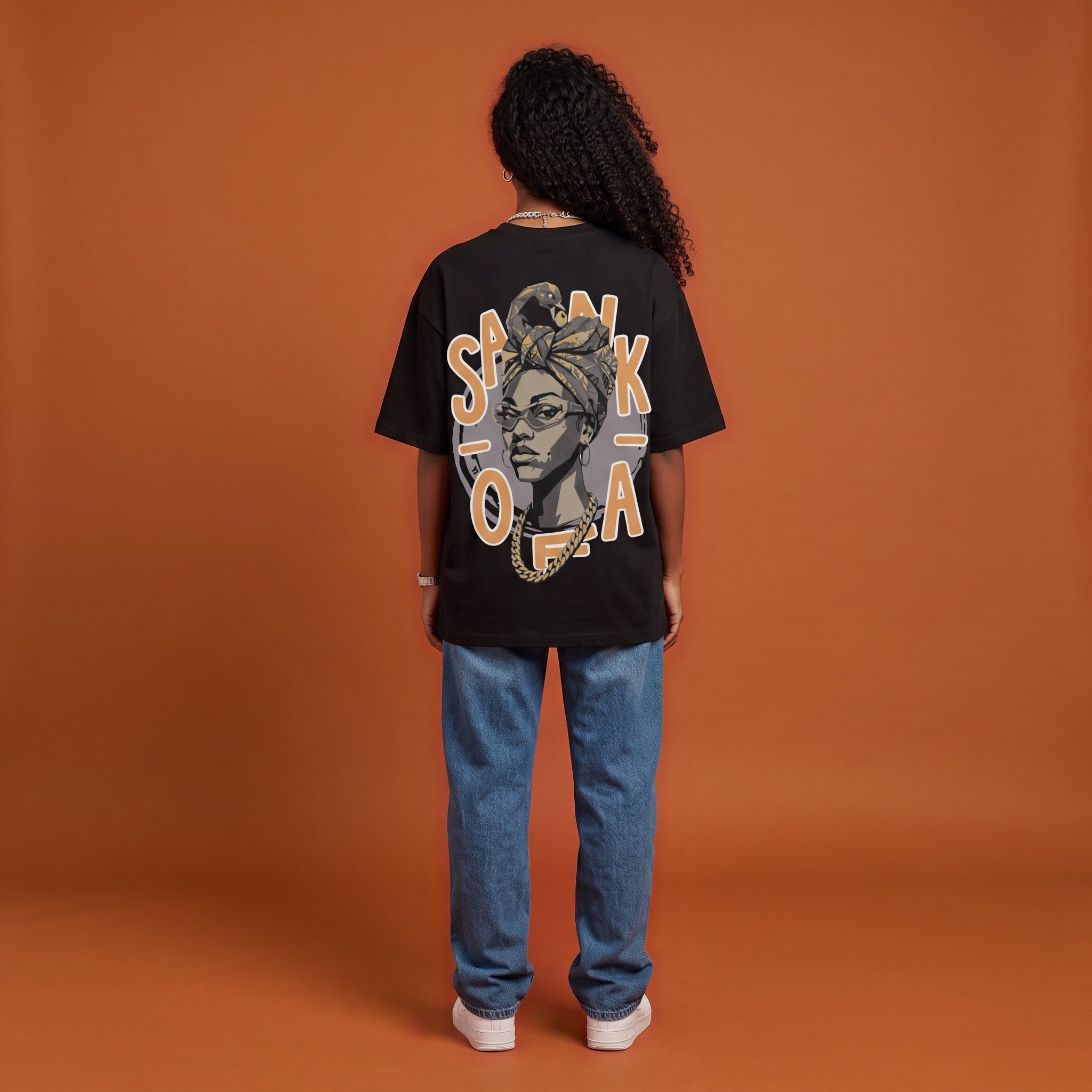 Blackness Sankofa Queen Tee, black, worn by a model — back view, Sankofa headwrap portrait print, terracotta backdrop