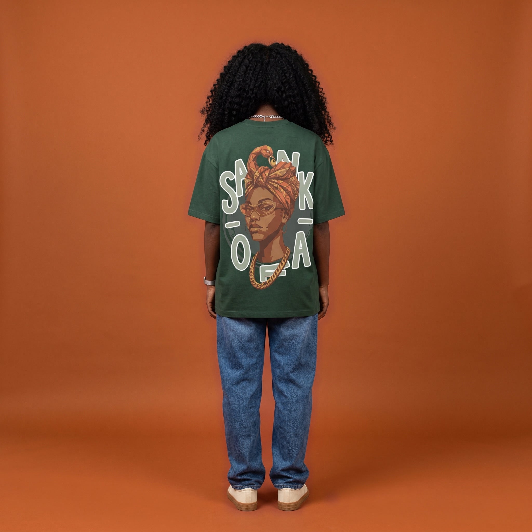 Blackness Sankofa Queen Tee, deep forest green, worn by a model — back view, Sankofa headwrap portrait print, terracotta backdrop