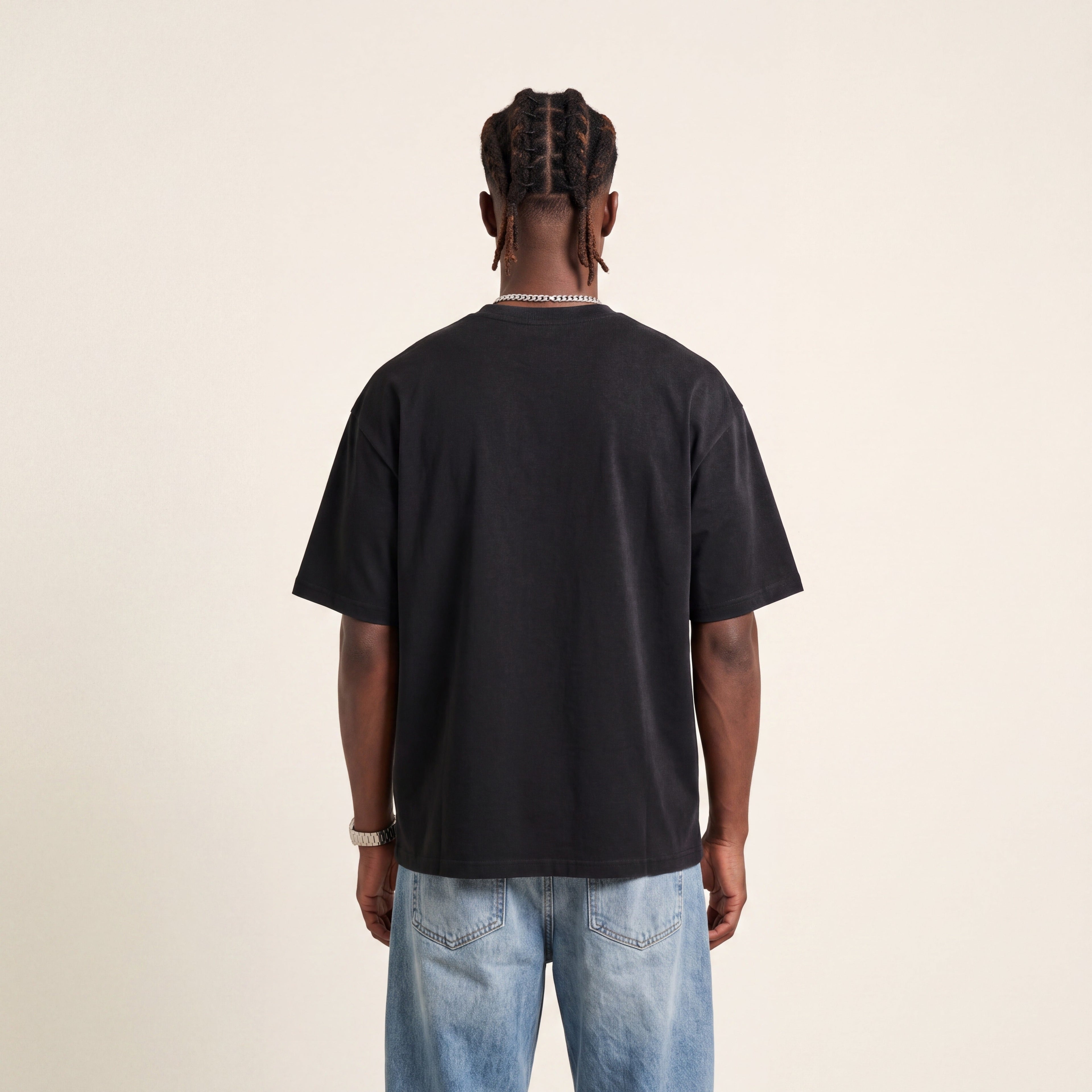 Base Blackness Tee Black worn by model, back view showing the clean plain back on warm ivory studio backdrop