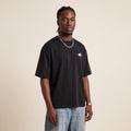 Base Blackness Tee Black worn by model, front view with WB chest logo on warm ivory studio backdrop