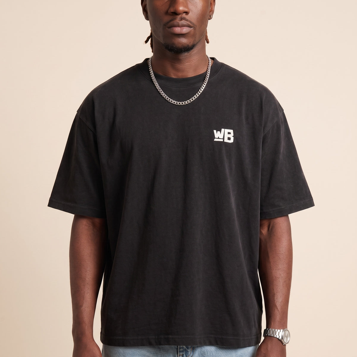 Blackness Emancipation Tee Black — close-up of the WB monogram chest logo and ribbed collar, oversized heavyweight cotton streetwear tee by We Are Blackness