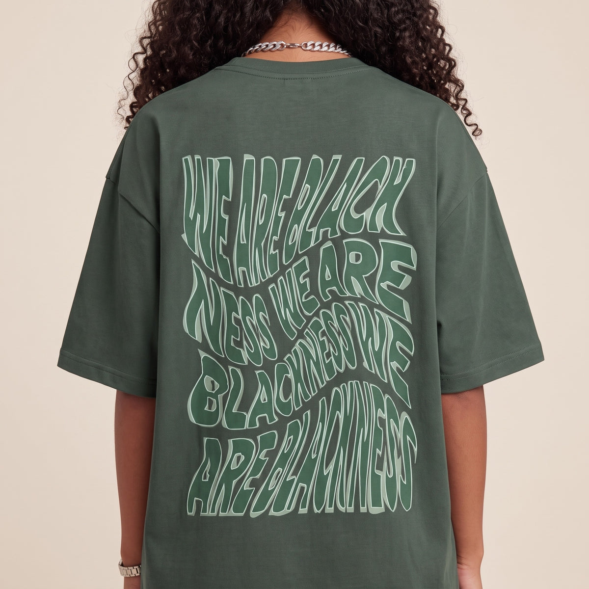 Blackness Honor & Embrace Tee Cactus Green — close-up of the wavy We Are Blackness typography back print worn on the back, oversized heavyweight cotton streetwear tee by We Are Blackness