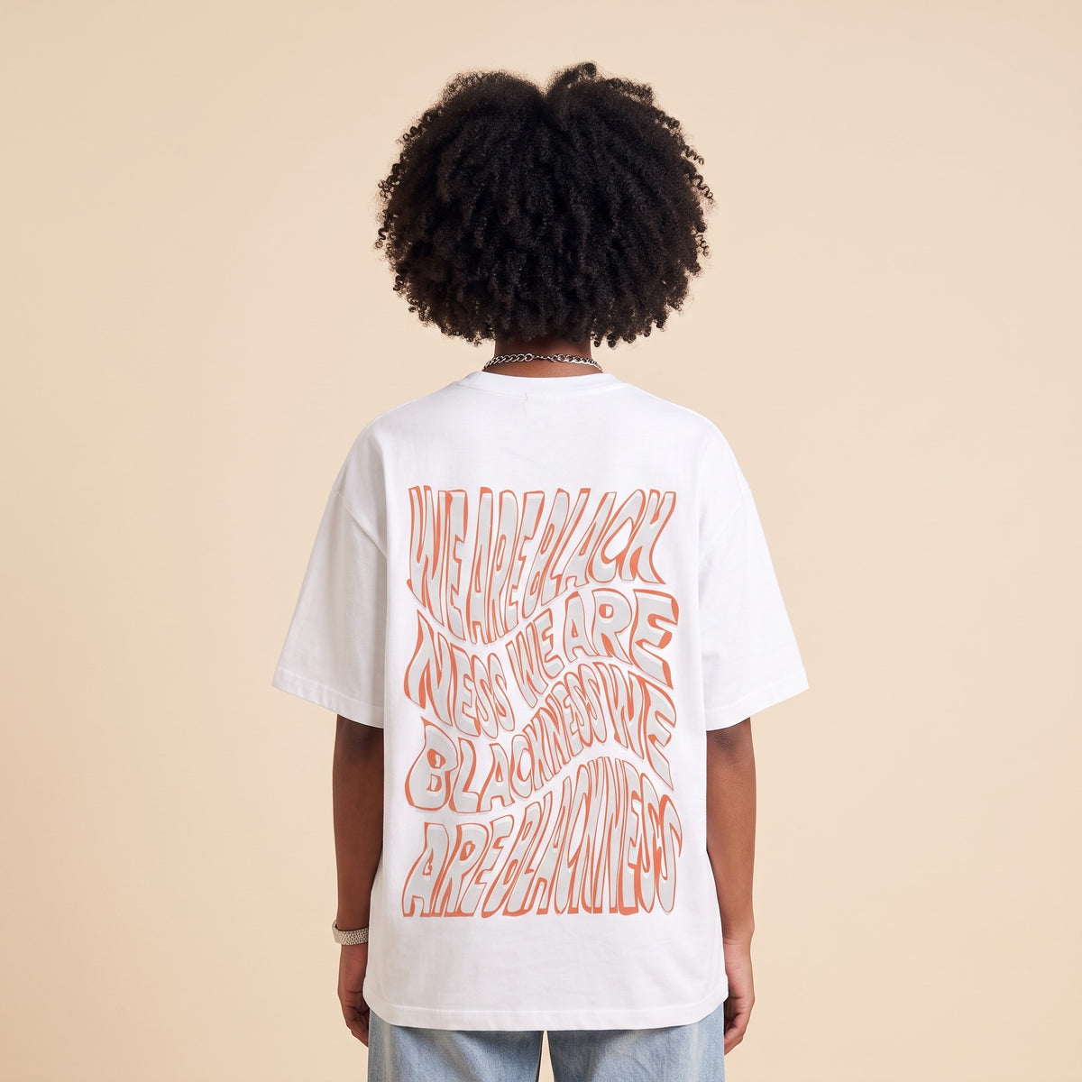 Blackness Honor & Embrace Tee White — close-up of the wavy We Are Blackness typography back print worn on the back, oversized heavyweight cotton streetwear tee by We Are Blackness