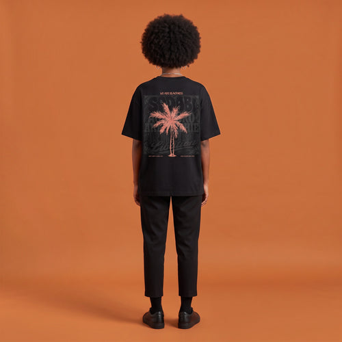 Blackness Libation Tee, black, worn by a model — back view, palm tree Libation print, terracotta-orange studio backdrop