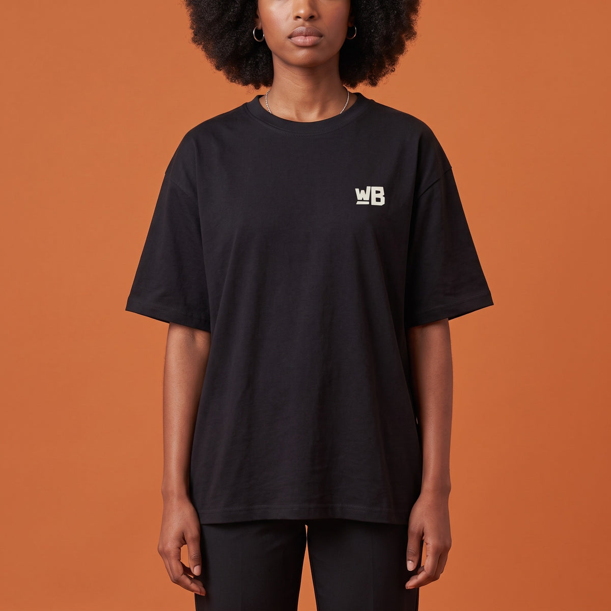 Blackness Libation Tee Black — close-up of the WB monogram chest logo and ribbed collar, oversized heavyweight cotton streetwear tee by We Are Blackness