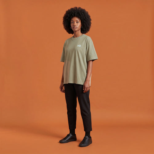 Blackness Libation Tee, brown khaki, worn by a model — front view with WB chest logo, terracotta-orange studio backdrop