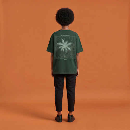 Blackness Libation Tee, forest green, worn by a model — back view, palm tree Libation print, terracotta-orange studio backdrop