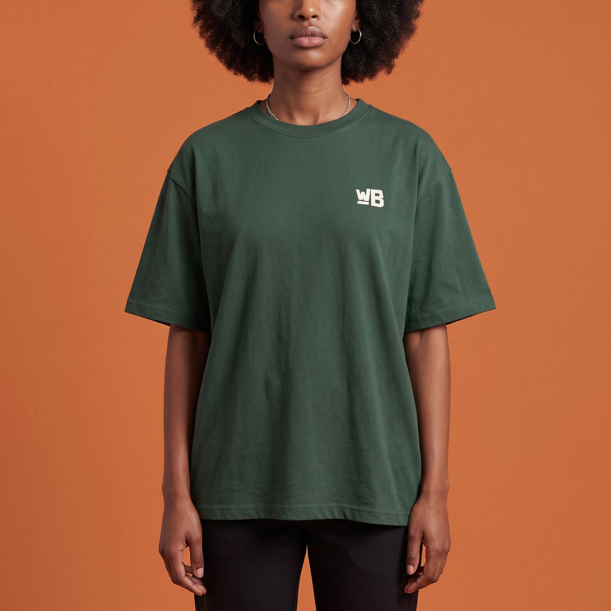 Blackness Libation Tee Forest Green — close-up of the WB monogram chest logo and ribbed collar, oversized heavyweight cotton streetwear tee by We Are Blackness