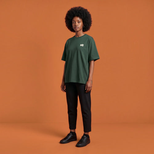 Blackness Libation Tee, forest green, worn by a model — front view with WB chest logo, terracotta-orange studio backdrop