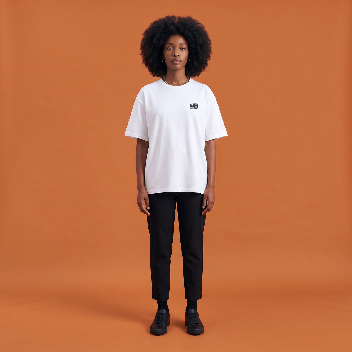 Blackness Libation Tee, white, worn by a model — front view with WB chest logo, terracotta-orange studio backdrop
