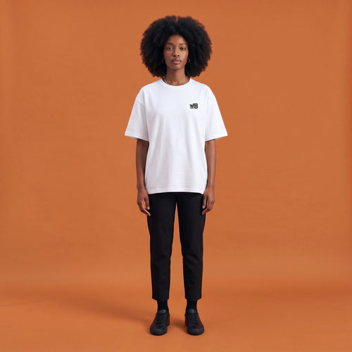 Blackness Libation Tee, white, worn by a model — front view with WB chest logo, terracotta-orange studio backdrop