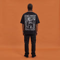 Blackness Mawon Tee, black, worn by a model — back view, Neg Mawon conch-blower block print, terracotta-orange studio backdrop
