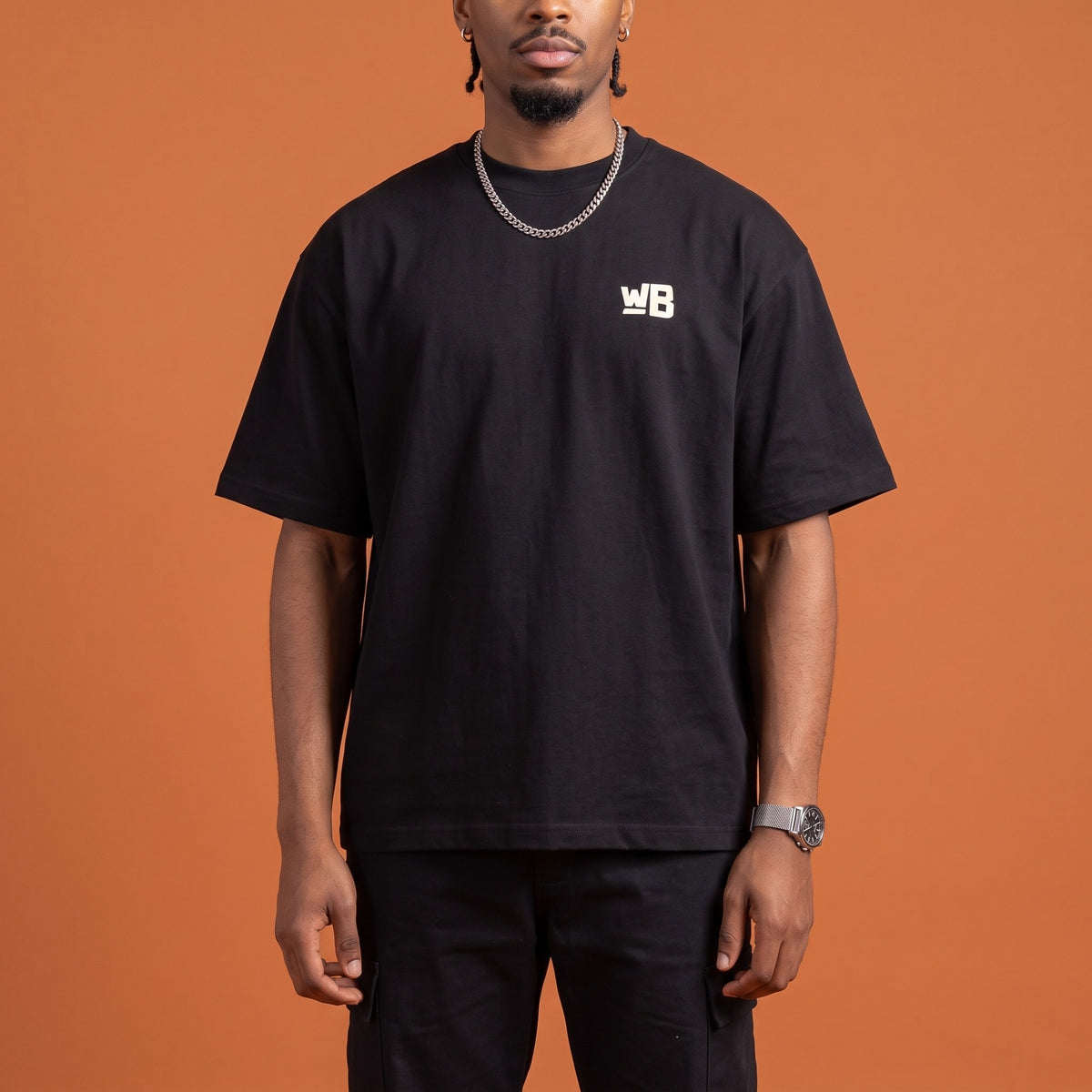 Blackness Mawon Tee Black — close-up of the WB monogram chest logo and ribbed collar, oversized heavyweight cotton streetwear tee by We Are Blackness
