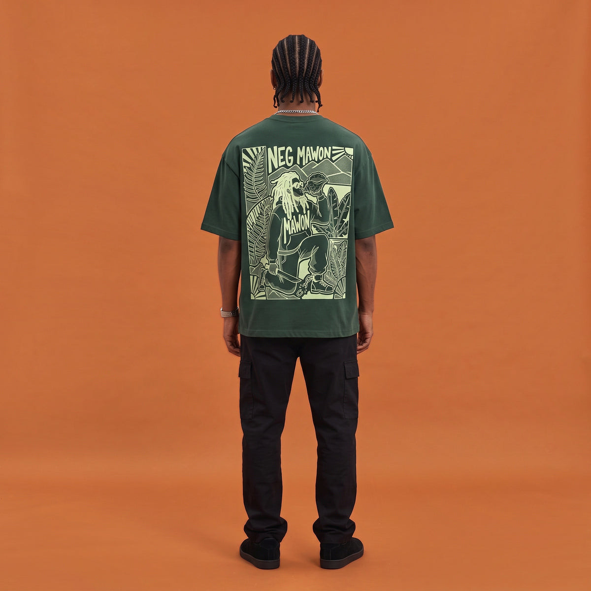 Blackness Mawon Tee, forest green, worn by a model — back view, Neg Mawon conch-blower block print, terracotta-orange studio backdrop