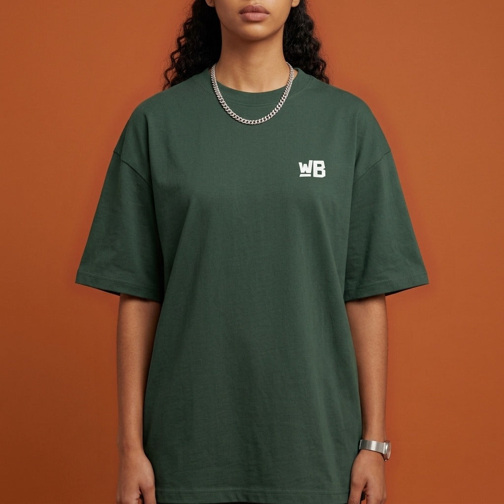 Blackness Sankofa Queen Tee, deep forest green — chest detail close-up with WB monogram and ribbed collar, terracotta backdrop