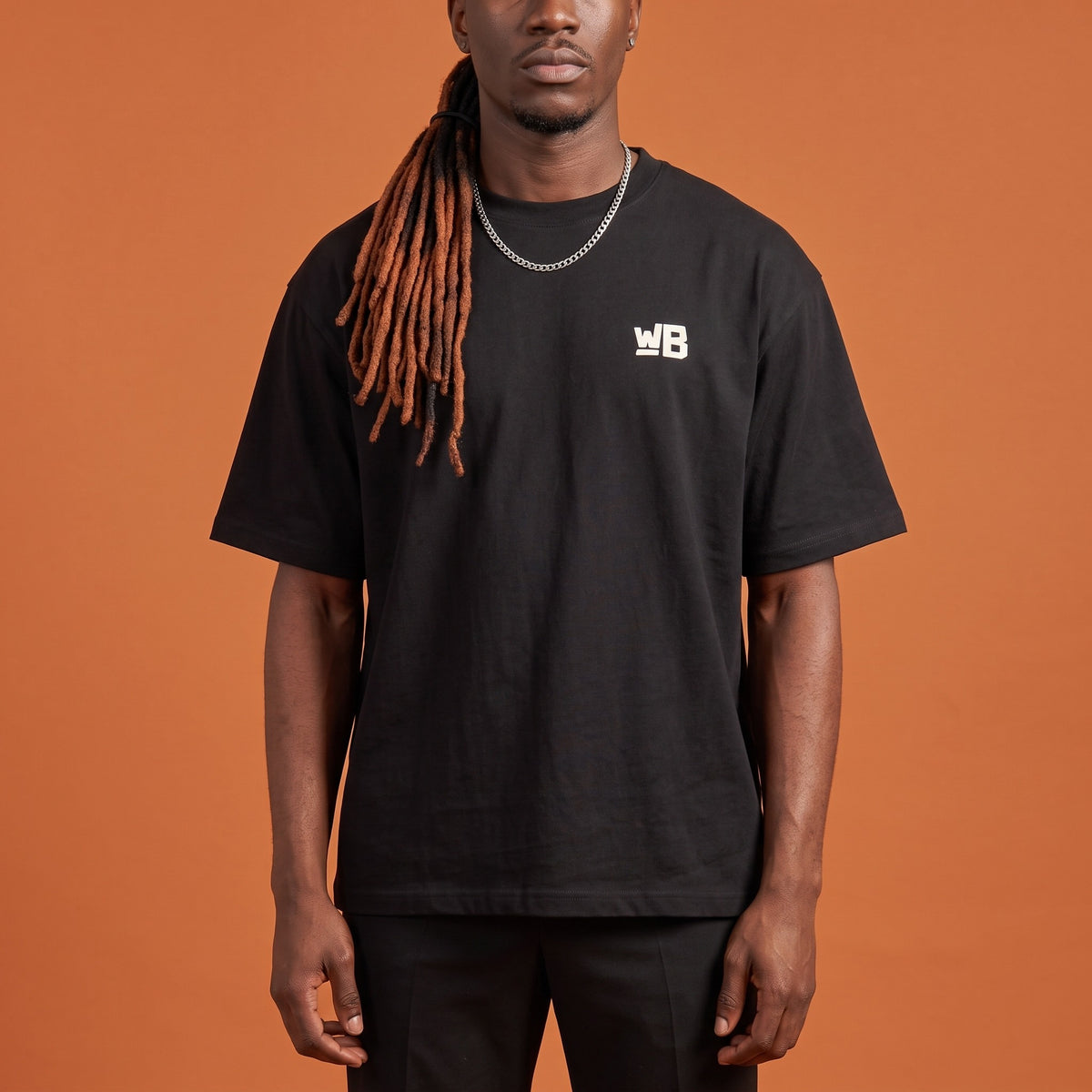 Blackness Sodabi Tee Black — close-up of the WB monogram chest logo and ribbed collar, oversized heavyweight cotton streetwear tee by We Are Blackness