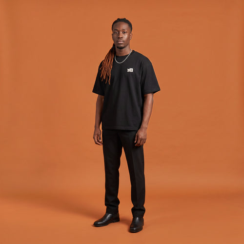 Blackness Sodabi Tee, black, worn by a model — front view with WB chest logo, terracotta-orange studio backdrop