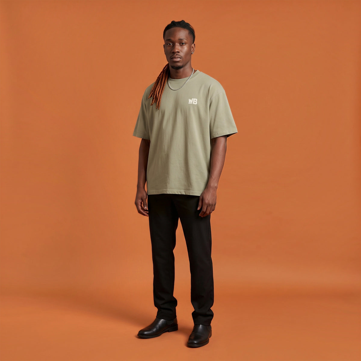 Blackness Sodabi Tee, brown khaki, worn by a model — front view with WB chest logo, terracotta-orange studio backdrop