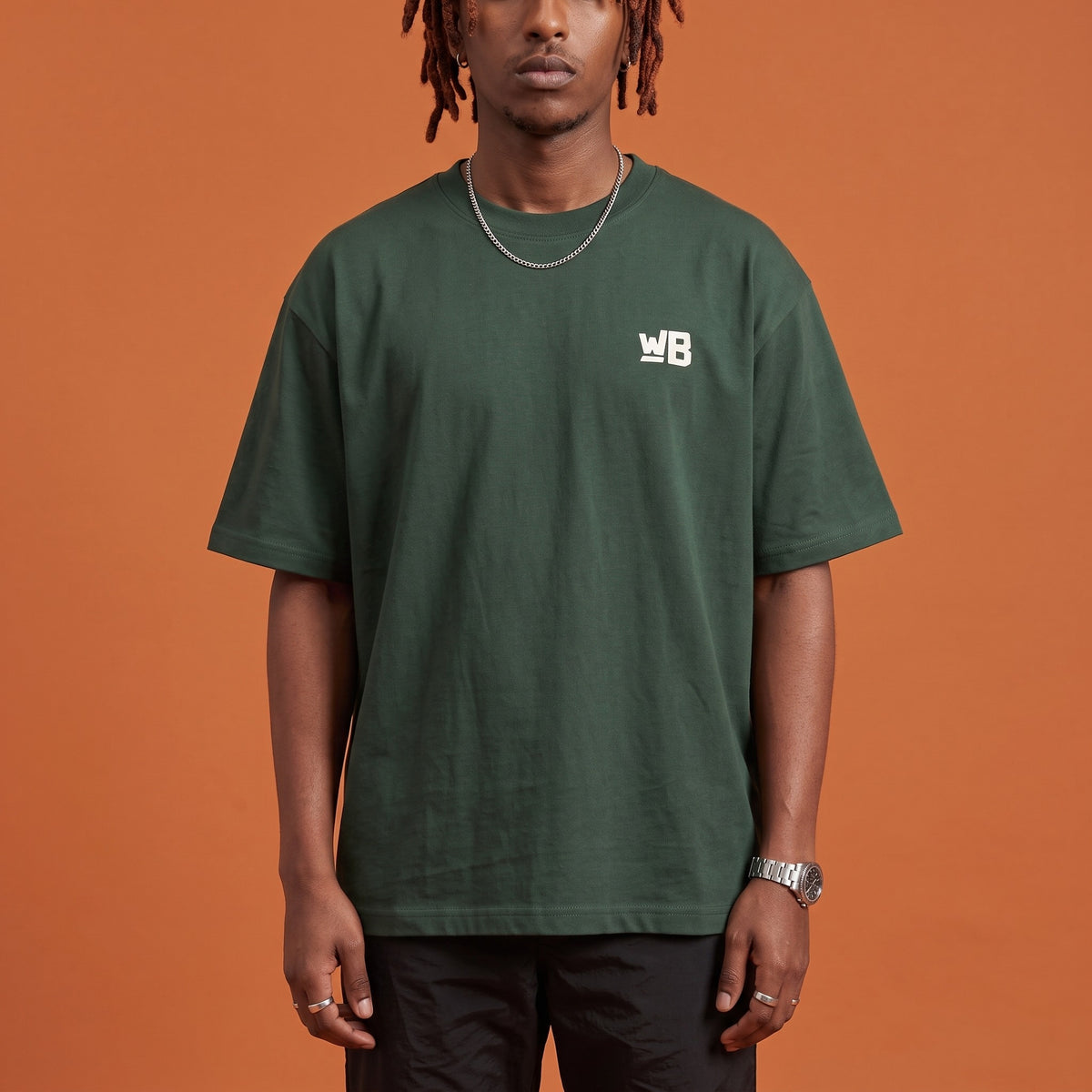 Blackness Sodabi Tee Forest Green — close-up of the WB monogram chest logo and ribbed collar, oversized heavyweight cotton streetwear tee by We Are Blackness