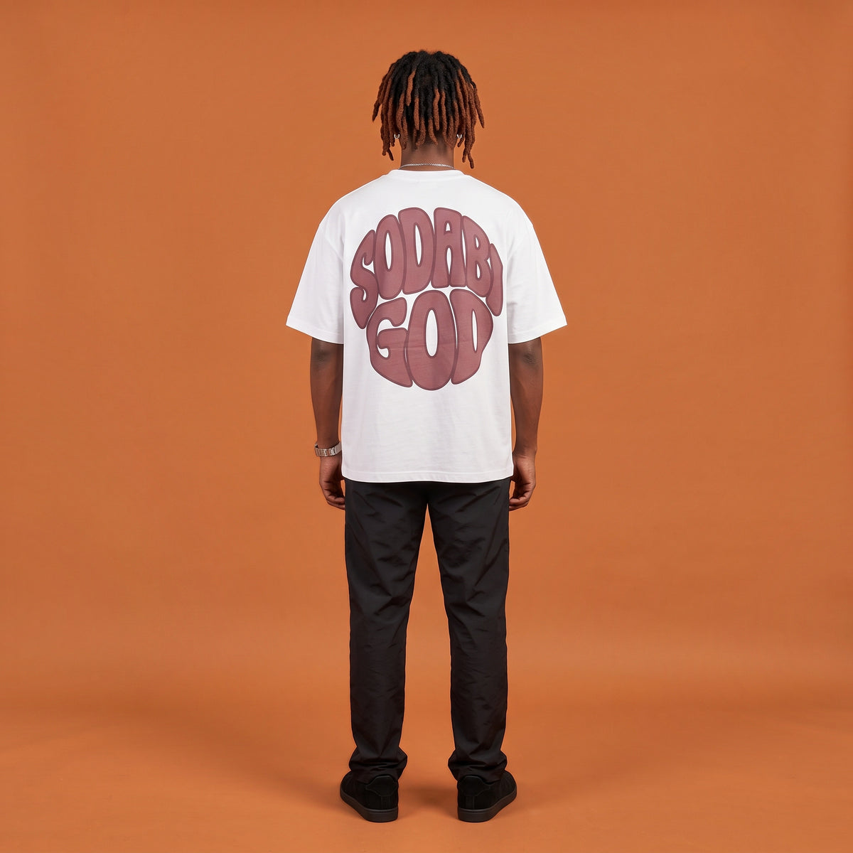 Blackness Sodabi Tee, white, worn by a model — back view, SODABI GOD bubble lettering print, terracotta-orange studio backdrop