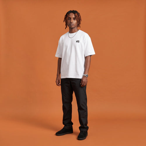 Blackness Sodabi Tee, white, worn by a model — front view with WB chest logo, terracotta-orange studio backdrop