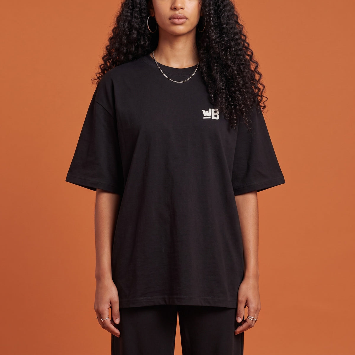 Blackness Solitude Tee Black — close-up of the WB monogram chest logo and ribbed collar, oversized heavyweight cotton streetwear tee by We Are Blackness