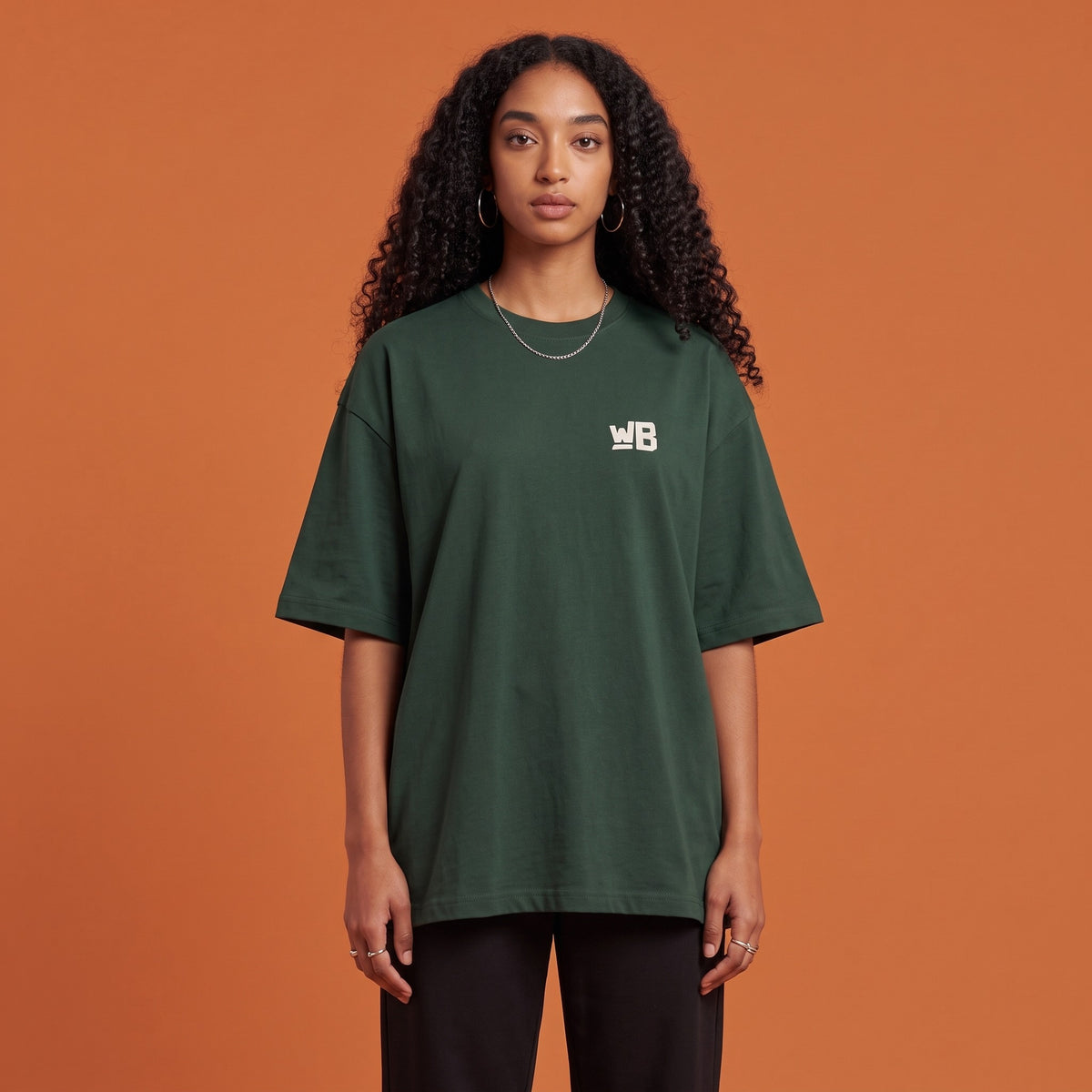 Blackness Solitude Tee Forest Green — close-up of the WB monogram chest logo and ribbed collar, oversized heavyweight cotton streetwear tee by We Are Blackness