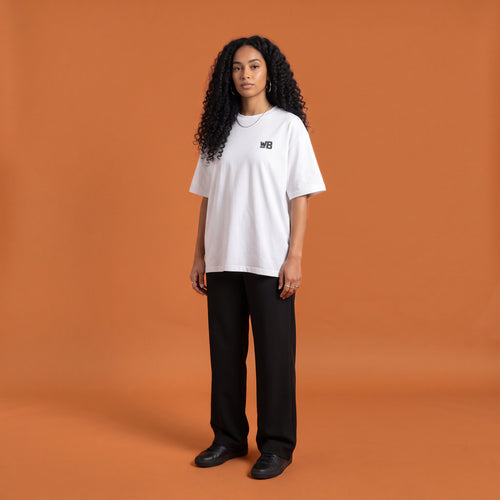 Blackness Solitude Tee, white, worn by a model — front view with WB chest logo, terracotta-orange studio backdrop