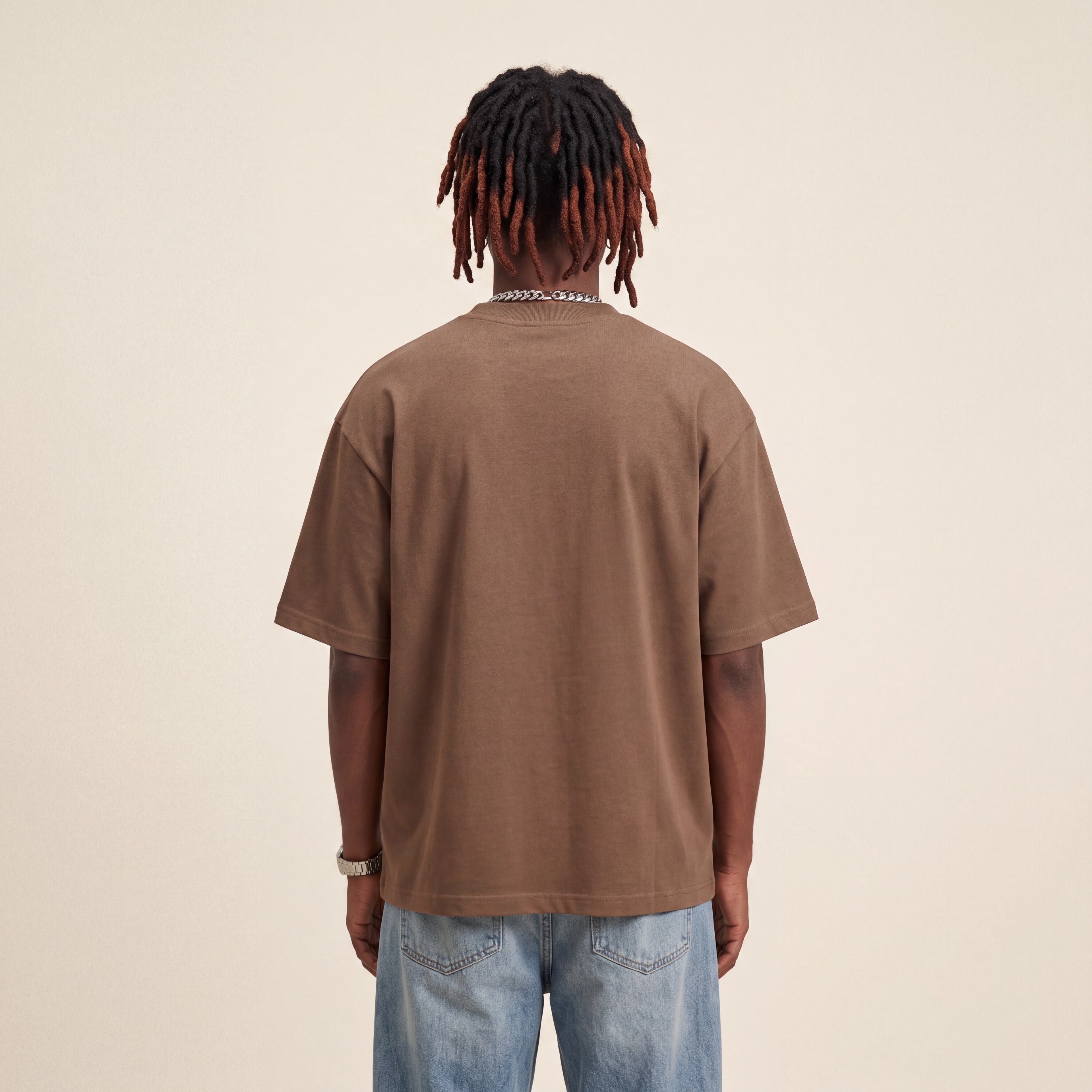 Base Blackness Tee Brown worn by model, back view showing the clean plain back on warm ivory studio backdrop
