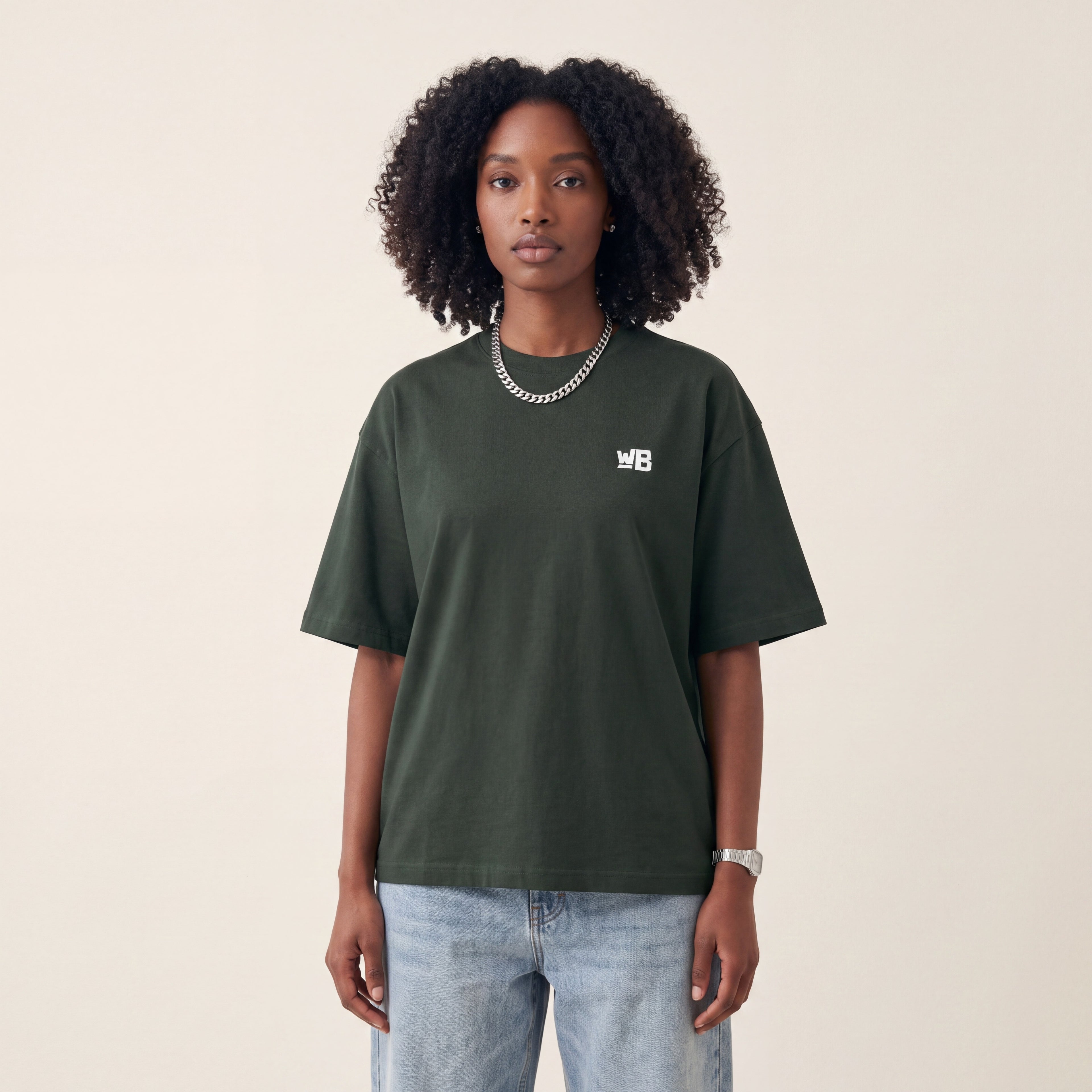 Base Blackness Tee Green worn by model, front view with WB chest logo on warm ivory studio backdrop