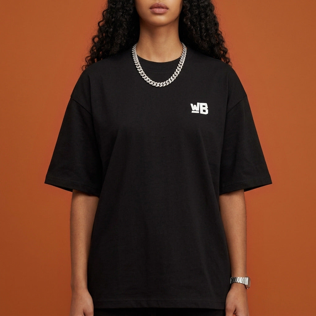 Blackness Sankofa Queen Tee, black — chest detail close-up with WB monogram and ribbed collar, terracotta backdrop