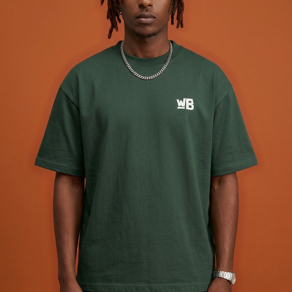 Blackness Sankofa King Tee, deep forest green — chest detail close-up with WB monogram and ribbed collar, terracotta backdrop