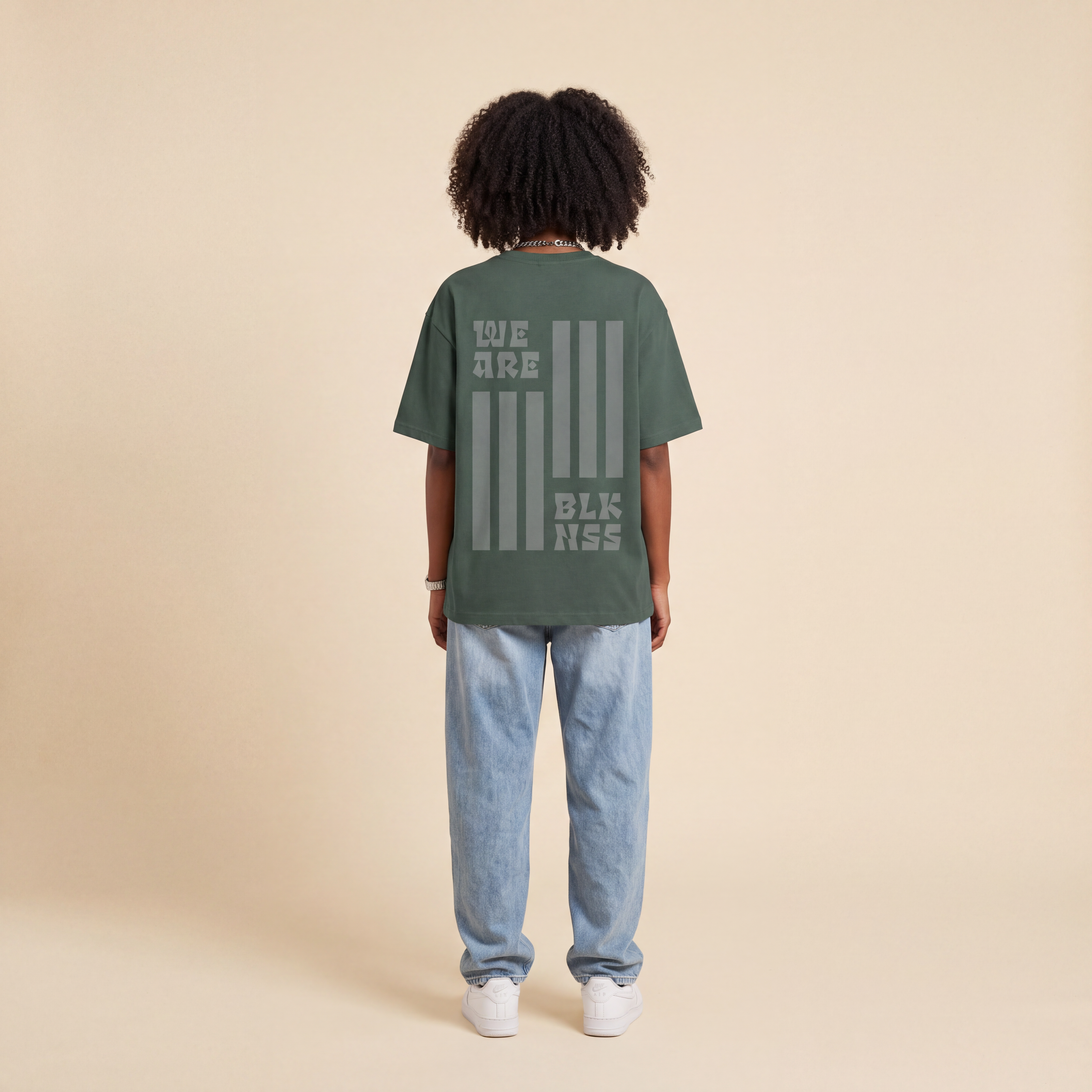 Blackness WABLKNSS Tee Green worn by model, back print view on beige studio backdrop