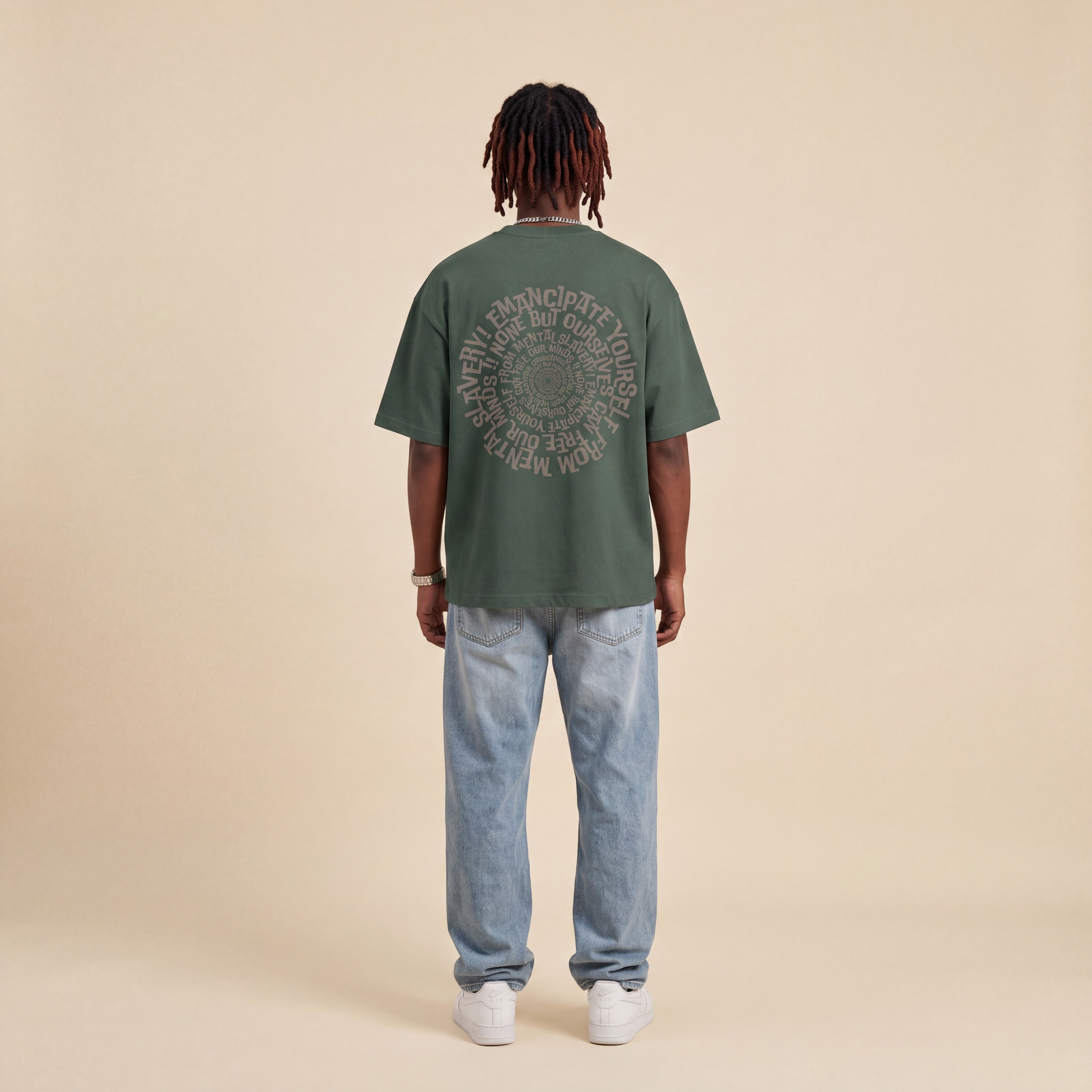 Blackness Emancipation Tee Cactus Green worn by model, back view showing the spiral Emancipate Yourself print on beige studio backdrop
