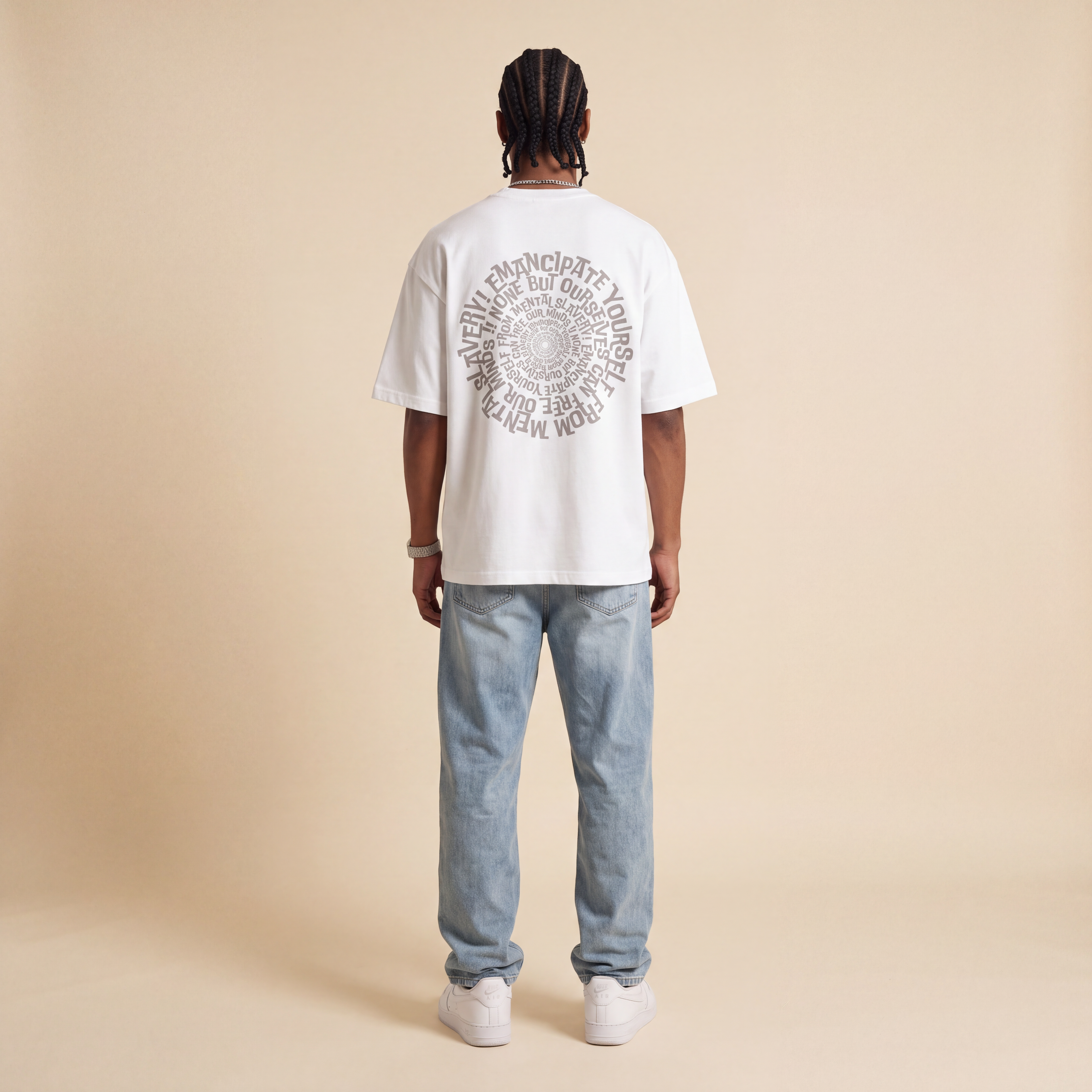 Blackness Emancipation Tee White worn by model, back view showing the spiral Emancipate Yourself print on beige studio backdrop