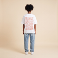 Blackness Honor & Embrace Tee White worn by model, back view showing the We Are Blackness wavy print on beige studio backdrop