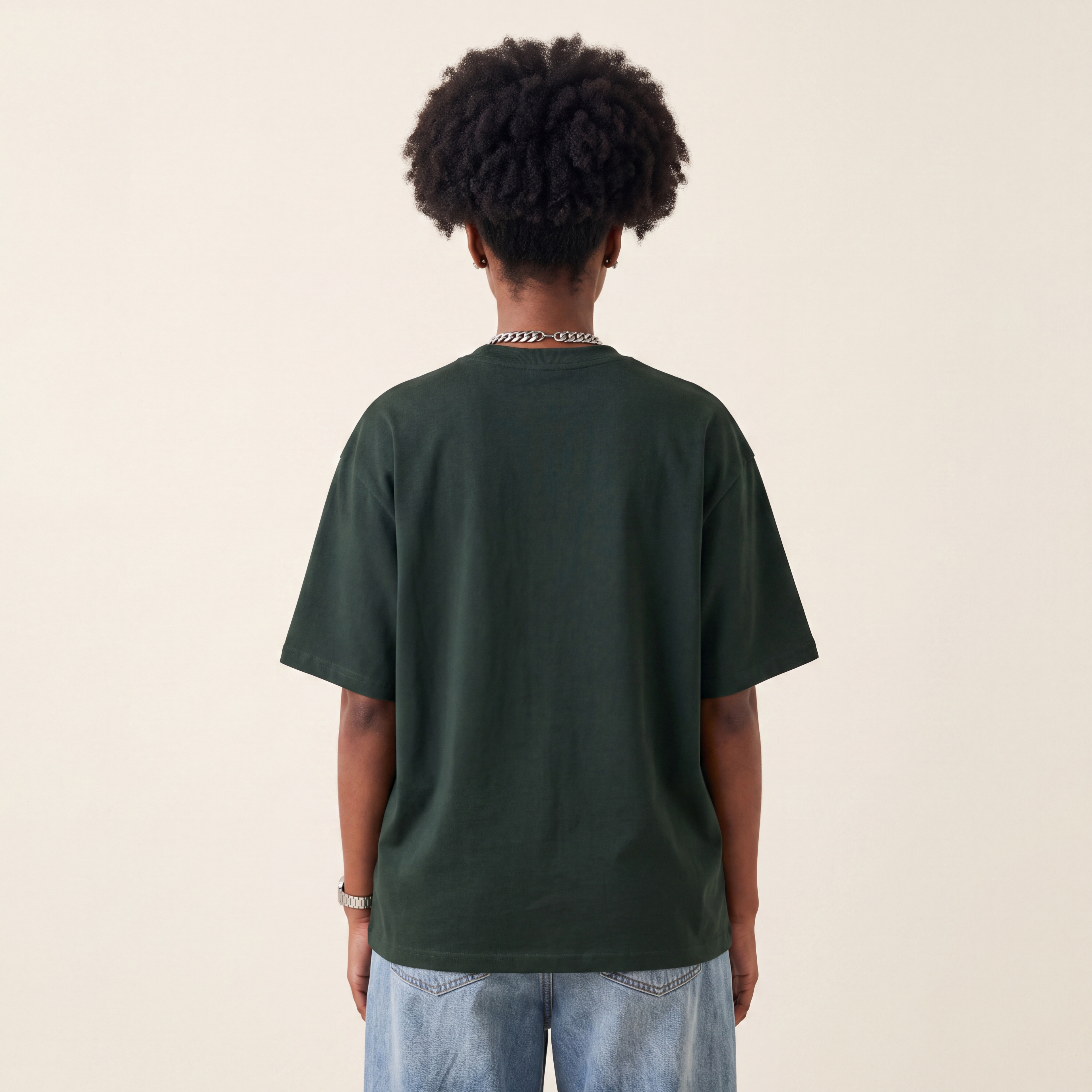 Base Blackness Tee Green worn by model, back view showing the clean plain back on warm ivory studio backdrop