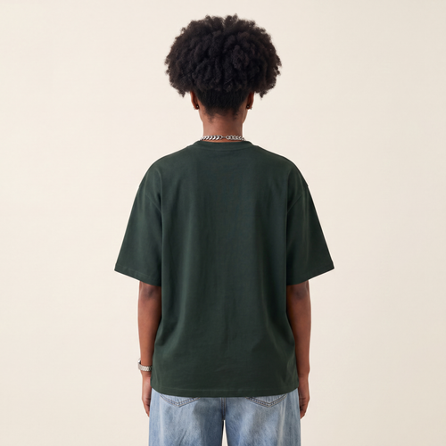 Base Blackness Tee Green worn by model, back view showing the clean plain back on warm ivory studio backdrop