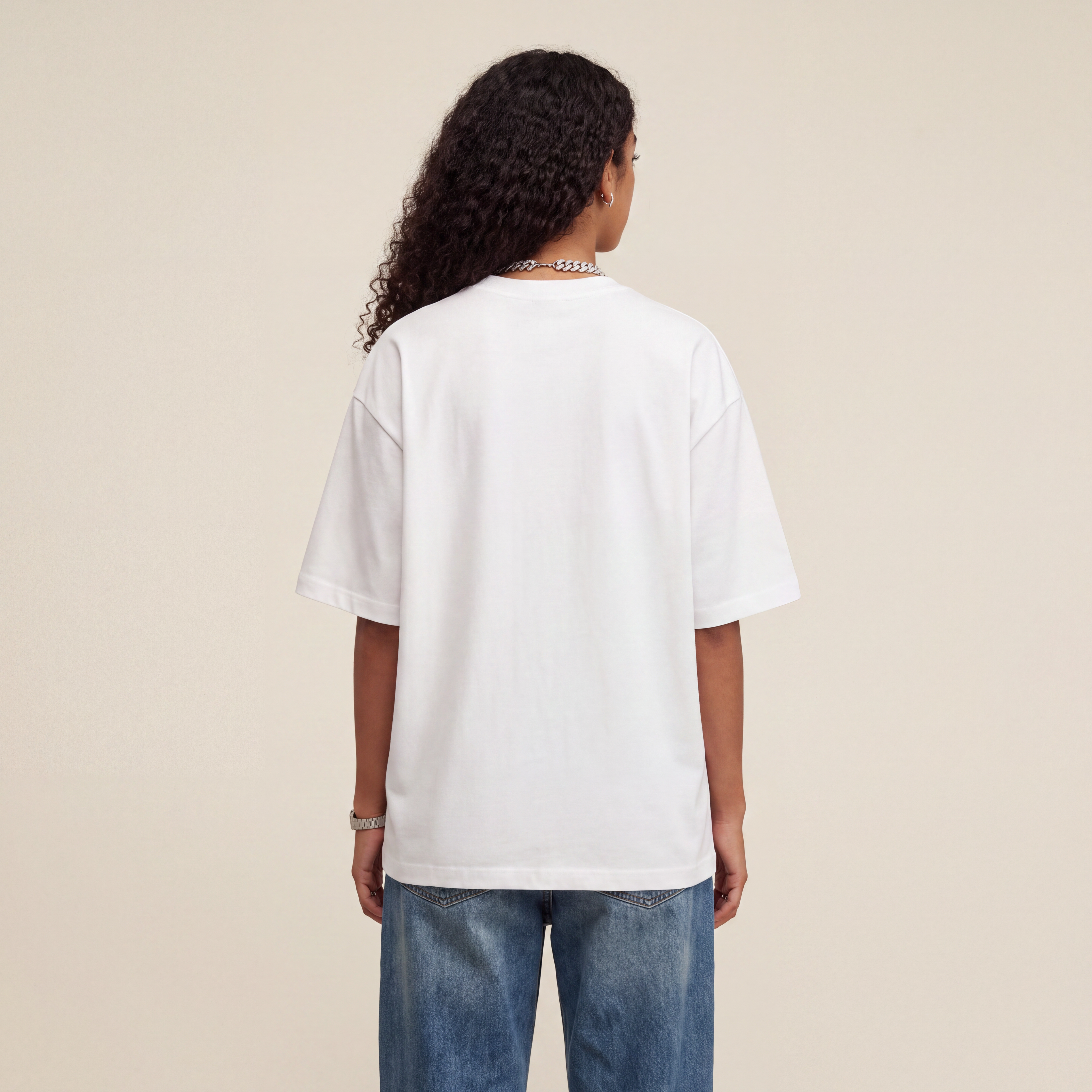 Base Blackness Tee White worn by model, back view showing the clean plain back on warm ivory studio backdrop